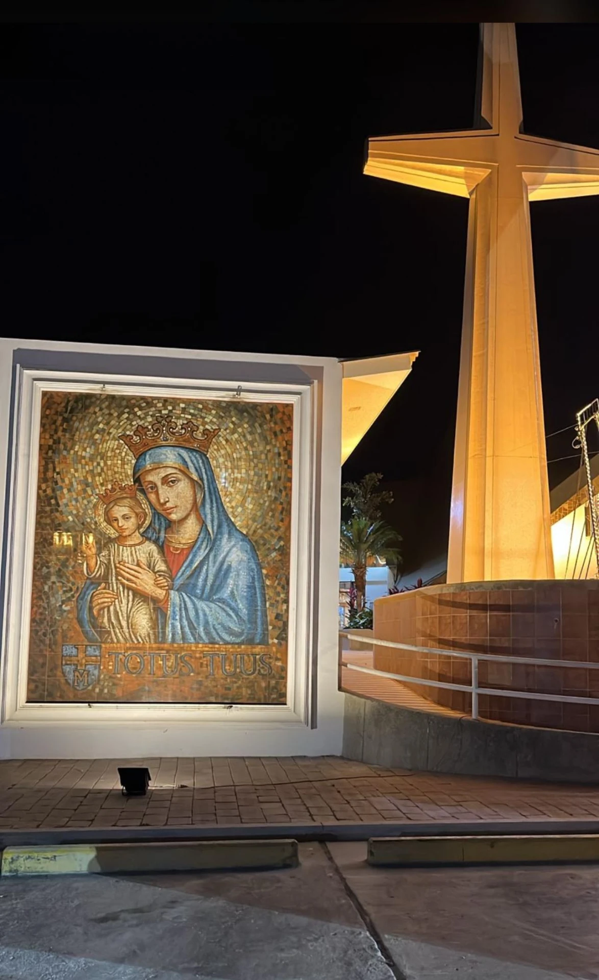 Mosaico de la Virgen María con el Niño Jesús con la inscripción Totus Tuus, y escultura de cruz monumental iluminada de noche