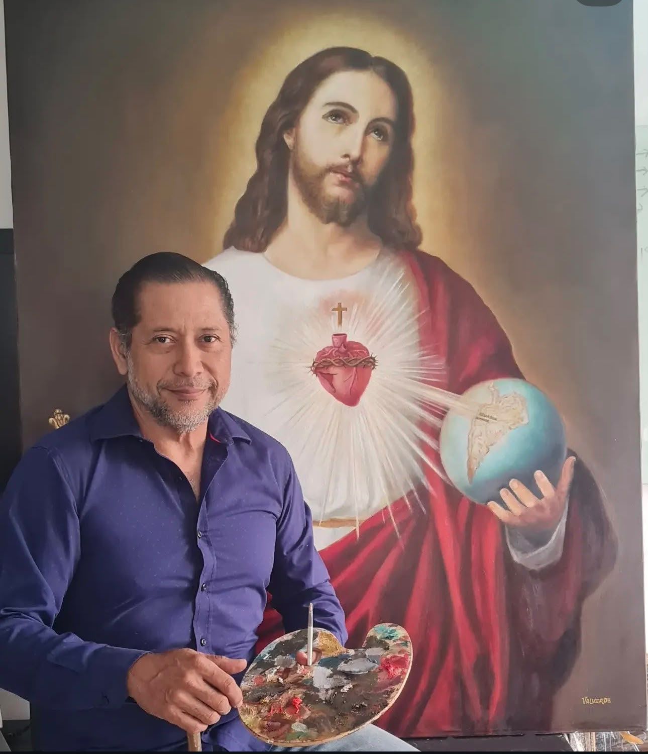 Fabricio Valverde, arquitecto, artista plástico y escultor, con paleta y pincel junto a su pintura del Sagrado Corazón